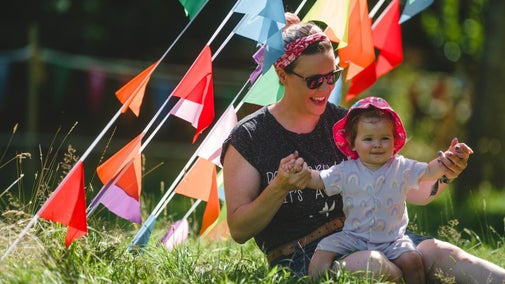 A mother and baby sitting on grass under multi-coloured bunting.